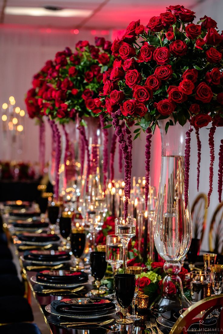 a long table is set with red roses and black place settings for an elegant dinner