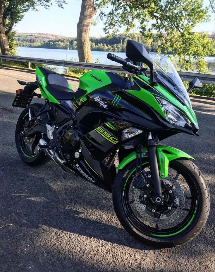 a green and black motorcycle parked on the side of a road next to a tree