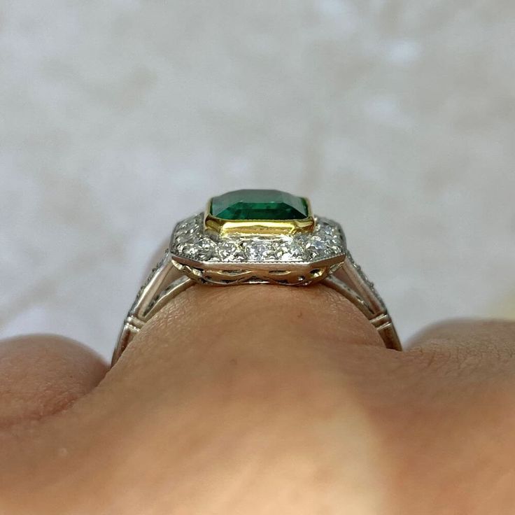 An emerald and diamond halo ring that centers a 1.48 carat emerald-cut natural emerald, bezel-set in gold. Surrounding the emerald and along the shoulders are old European cut diamonds. The total diamond weight is approximately 0.45 carats. This ring is 18k yellow gold on platinum, and decorated with an openwork under-gallery.
The measurements of the emerald are approximately 7.45mm x 6.19mm x 4.27mm. The ring including the diamond halo measures approximately 12.57mm x 11.24mm.
This ring can be Luxury Emerald Cut Emerald Ring With Halo Design, Luxury Radiant Cut Emerald Ring With Halo Setting, Luxury Emerald-cut Emerald Ring With Halo Design, Exquisite Emerald Cut Platinum Emerald Ring, Luxury Emerald Cut Gemstone Halo Ring, Emerald Ring With Asscher Cut Diamond And Bezel Setting, Emerald Ring With Bezel-set Asscher Cut Diamond, Green Emerald Cut Halo Ring In Platinum, Exquisite Emerald Cut Diamond Ring