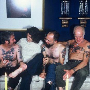 four men sitting on a couch with candles in their hands and tattoos on their arms