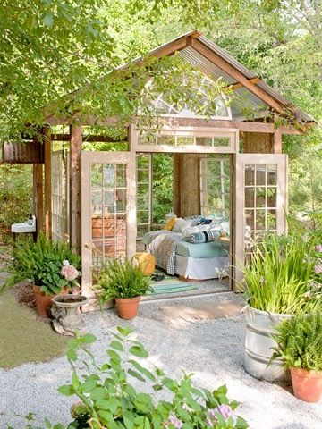 a garden shed with lots of potted plants and flowers in the foreground, surrounded by greenery