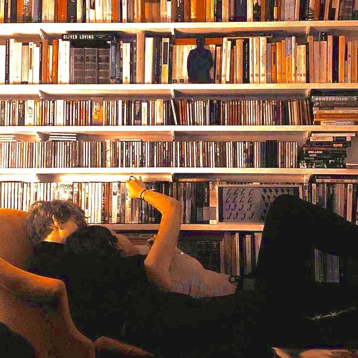 a woman laying on top of a couch in front of a book shelf filled with books