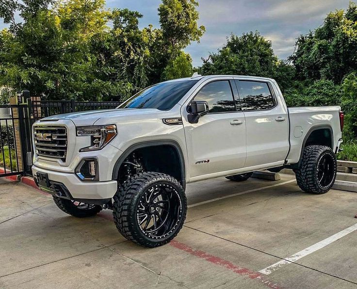 a white truck is parked in a parking lot next to a black fence and trees