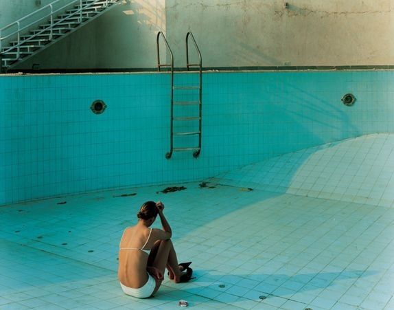 a woman sitting on the ground in front of a swimming pool with ladders above her head