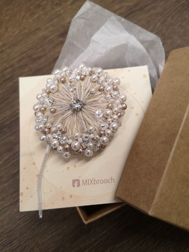 a close up of a brooch on a card next to a box with tissue paper