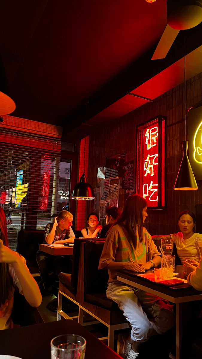 people sitting at tables in a restaurant with neon signs