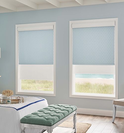 a bedroom with blue walls and two windows that have roman shades on them, along with a bench in front of the window