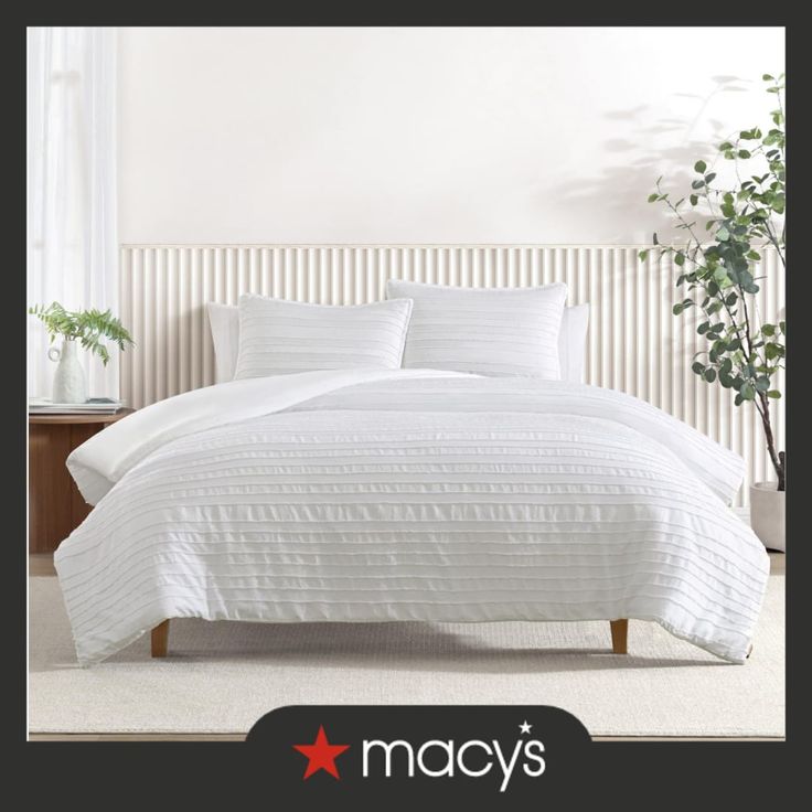 a bed with white comforter and pillows in a room next to a potted plant