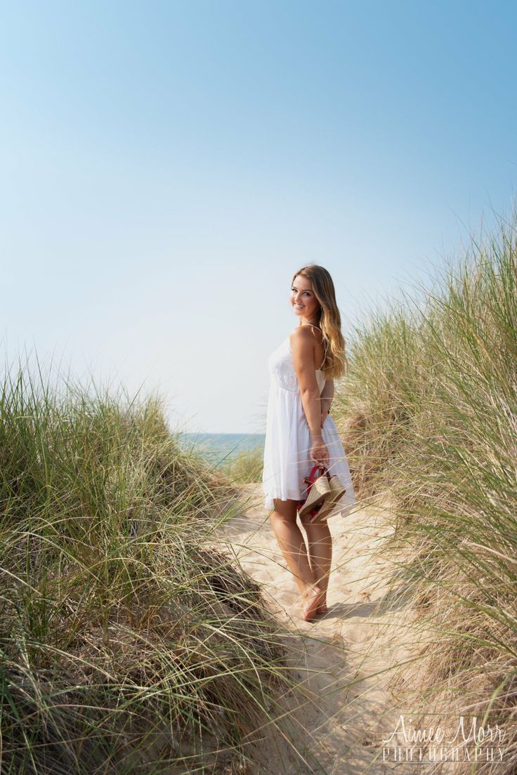 a woman standing on top of a sandy beach next to tall grass and sea oats