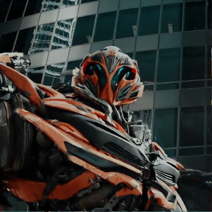 an orange and black robot standing in front of a tall building