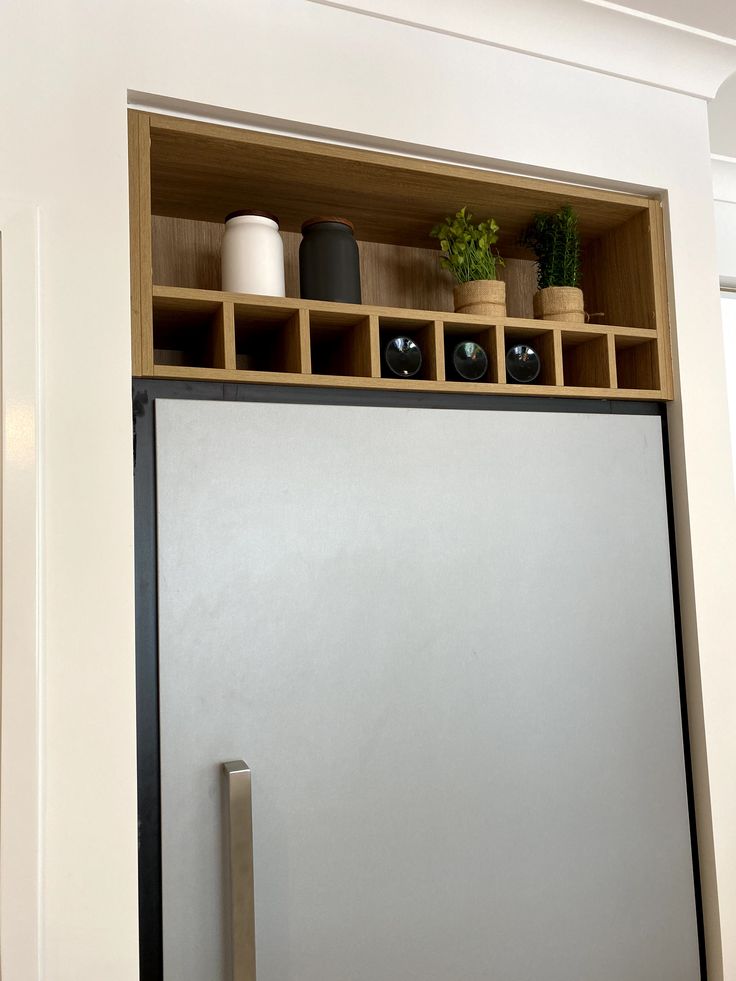 a refrigerator freezer sitting inside of a kitchen next to a wooden shelf filled with potted plants