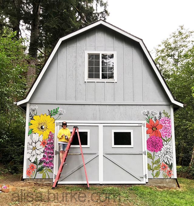 a man is painting the side of a barn with flowers on it and ladders