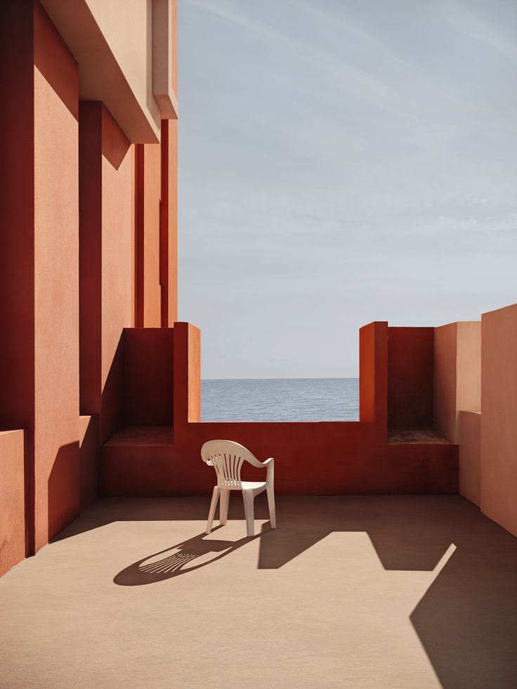 a white chair sitting on top of a cement floor next to a building near the ocean