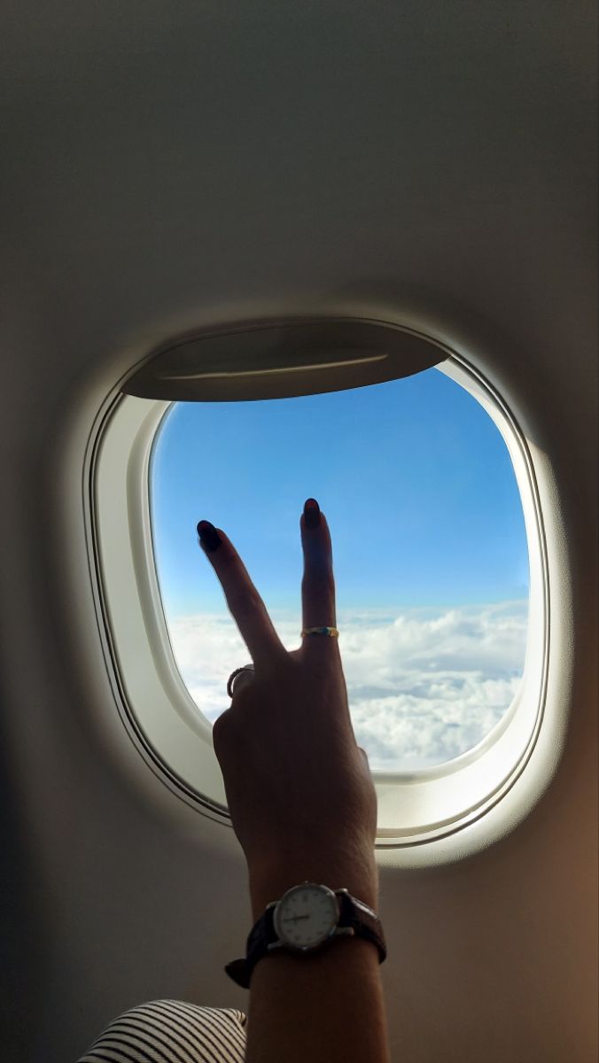 a person pointing at the sky through an airplane window with their finger in the air