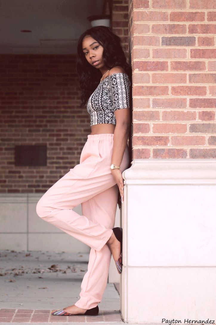 a woman leaning against a brick wall wearing pink pants