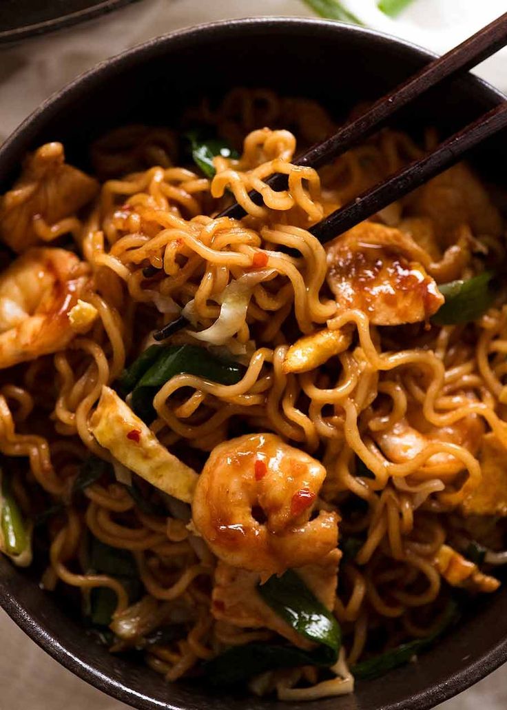 a bowl filled with noodles and shrimp on top of a wooden table next to chopsticks