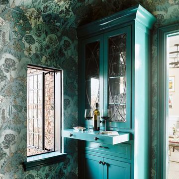 a green cabinet sitting next to a window in a room with wall paper on the walls