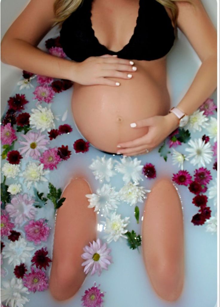 a pregnant woman sitting in a bathtub surrounded by flowers and daisies with her hands on her stomach