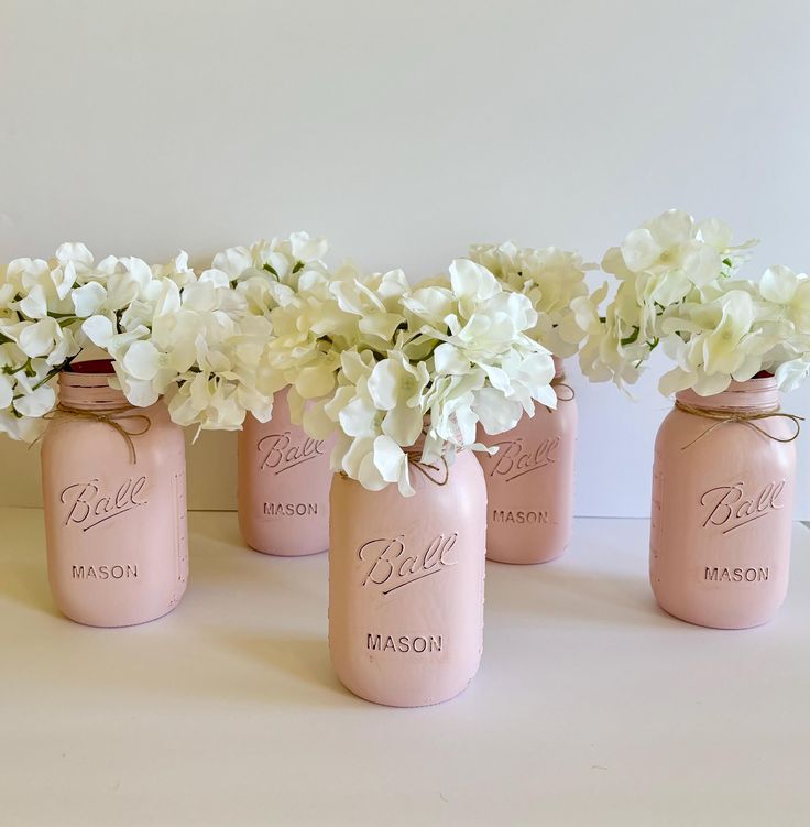 four pink mason jars with white flowers in them