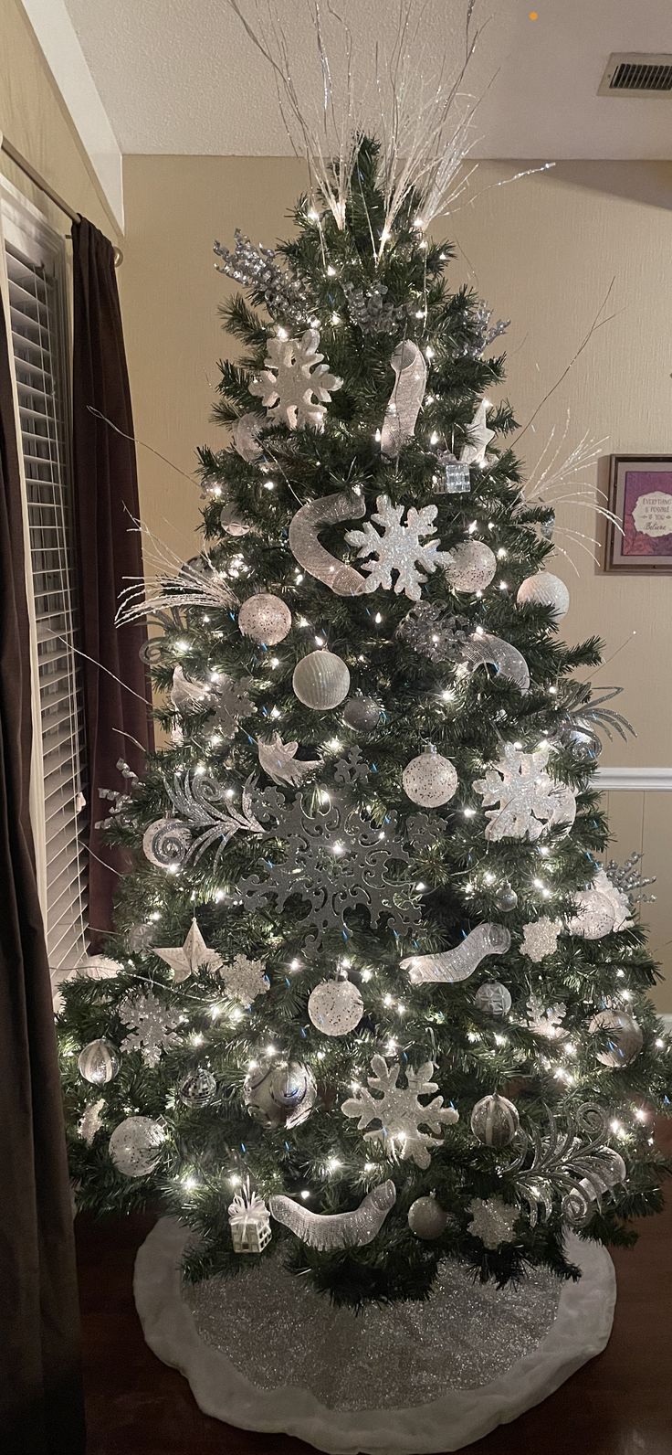 a white christmas tree with silver ornaments and snowflakes on it in a living room