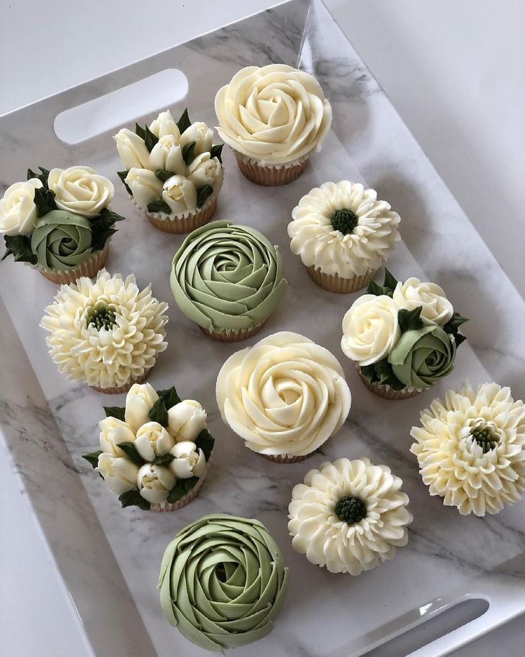 cupcakes decorated with white and green icing on a marble tray next to a knife