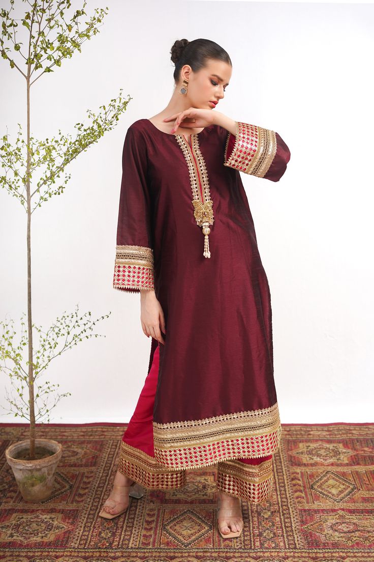 A maroon, raw silk, Kashmiri cut long kurta with Marori lace on the neck and sleeves. A pink tissue silk ajar pant lends a royal look to the suit. Finished with a matching tissue organza dupatta with pink border. 3-piece suit Ready to wear Bollywood Cotton Silk Palazzo Set With Embroidered Border, Tissue Silk Palazzo Set With Traditional Drape For Eid, Festival Tissue Silk Straight Kurta, Eid Tissue Silk Palazzo Set With Traditional Drape, Eid Tissue Silk Straight Kurta, Eid Tissue Silk Palazzo Set, Traditional Drape Art Silk Palazzo Set With Embroidered Border, Bollywood Style Tussar Silk Palazzo Set With Resham Embroidery, Traditional Embroidered Art Silk Palazzo Set