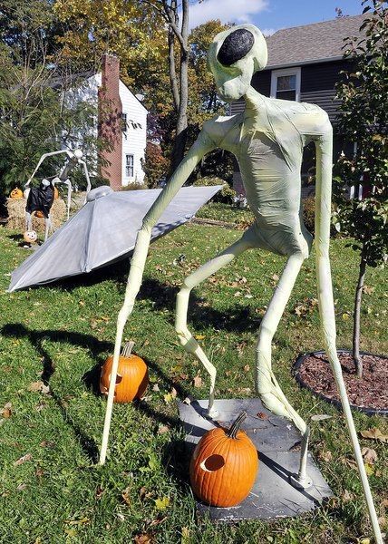 a statue of a skeleton with an umbrella and pumpkins on the ground in front of a house