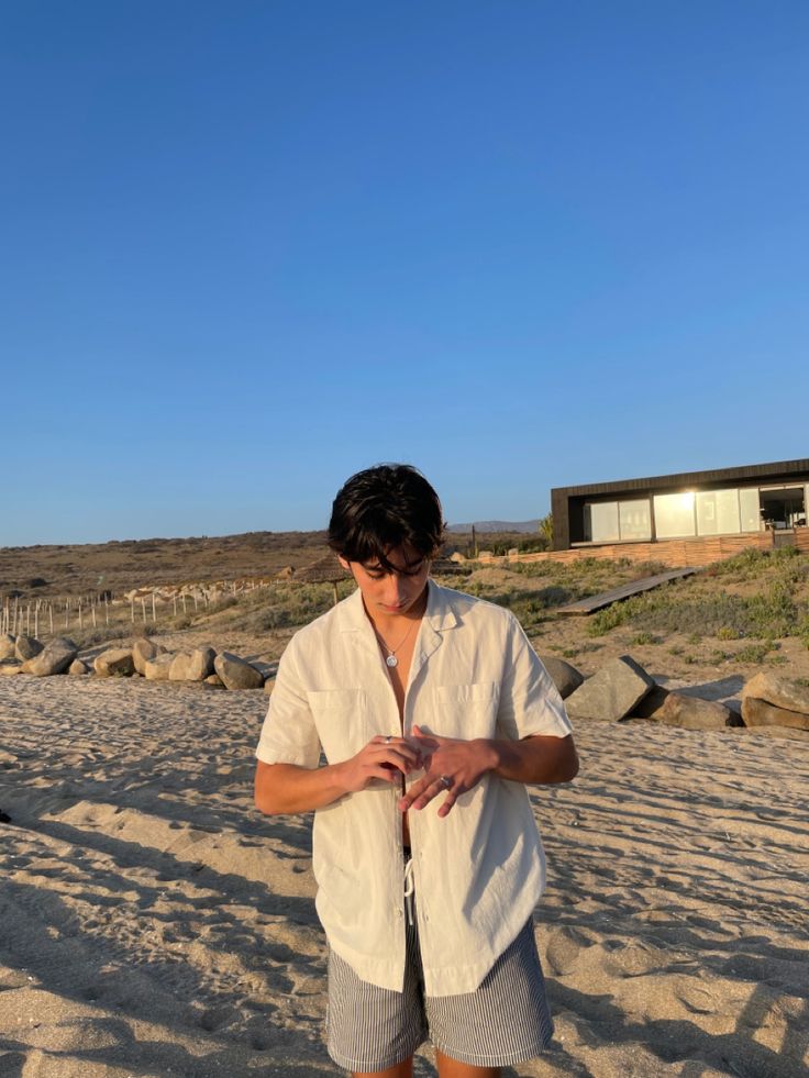 a man standing on top of a sandy beach next to the ocean with his hands in his pockets