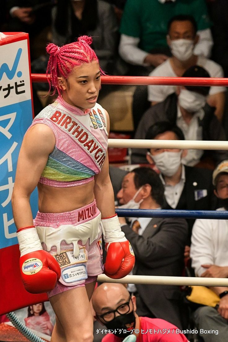 a woman with pink dreadlocks and boxing gloves walking in front of a crowd