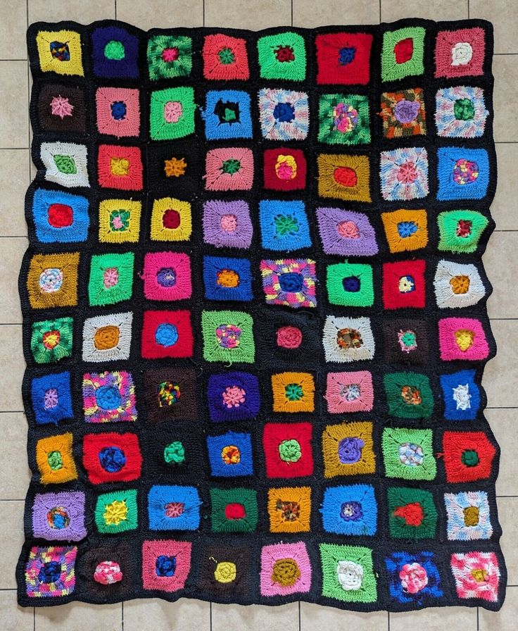 a crocheted blanket is on the floor in front of a tile wall with squares and flowers