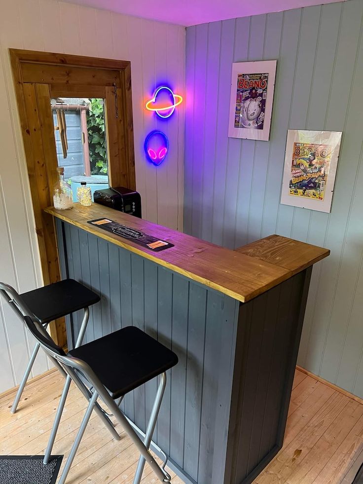 a bar with two stools in front of it and a neon sign on the wall