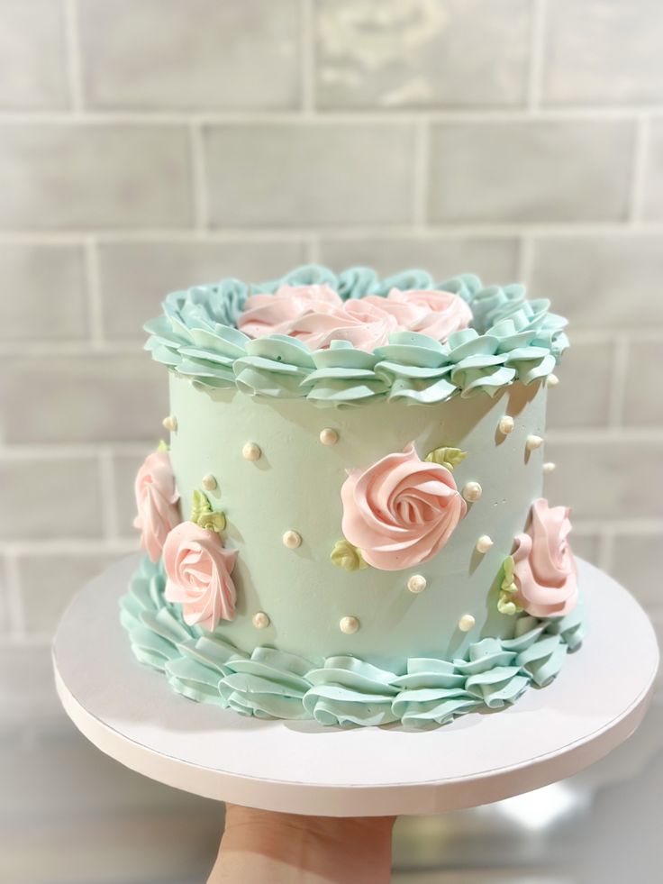 a hand holding a cake with frosting and flowers on the top, in front of a brick wall