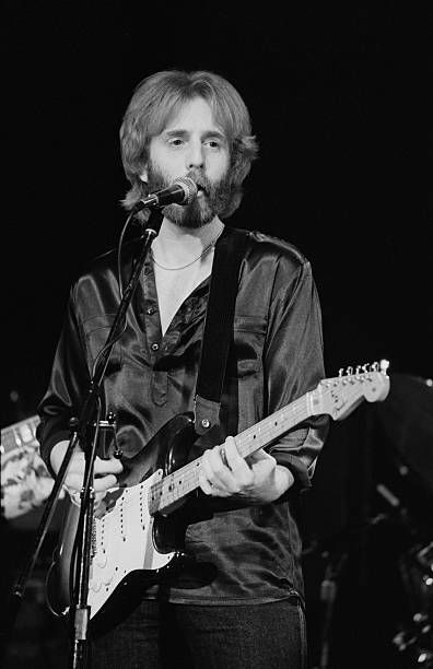 black and white photograph of man playing guitar on stage with microphone in front of him