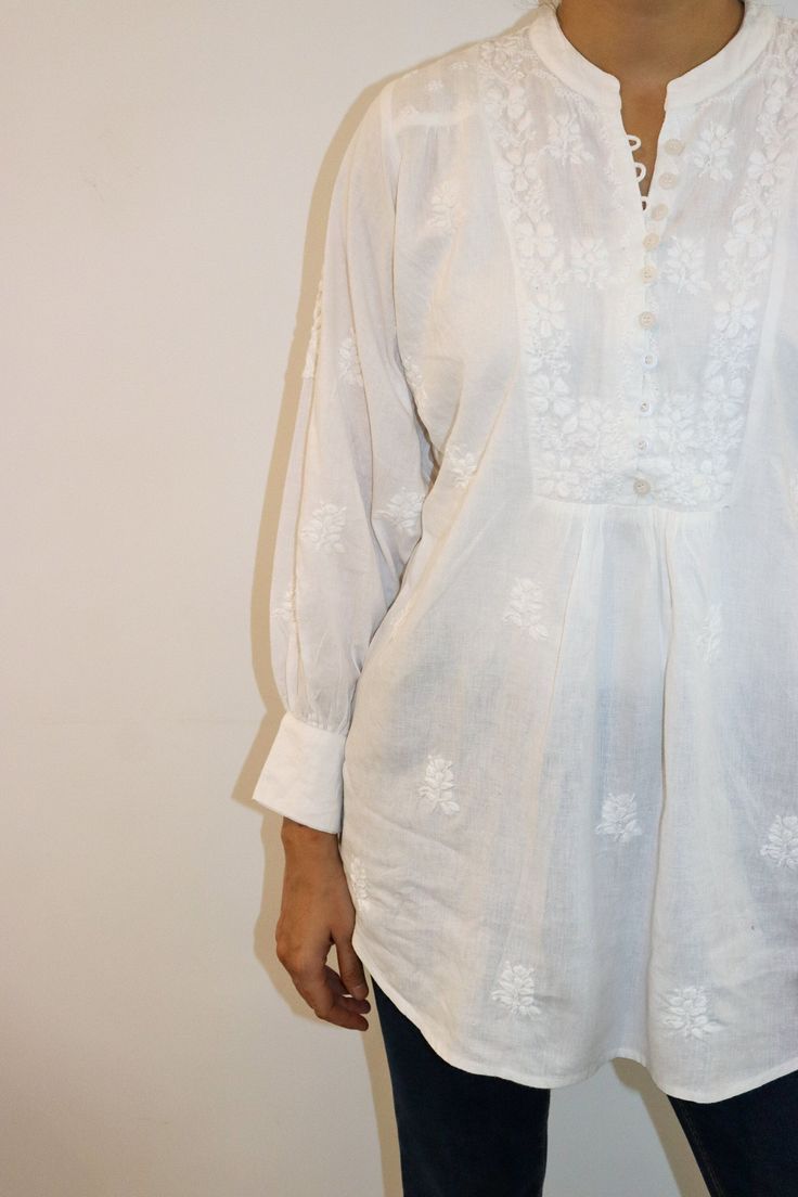 Step into effortless sophistication with our Timeless Elegance Linen Blouse. Crafted from the softest white linen, this blouse features exquisite vintage chikankari embroidery that whispers tales of heritage. The buttoned yoke, accentuated with delicate shoulder panels, adds a touch of classic charm. Cuffed poet sleeves complete the look, offering a flowy and romantic silhouette. Key Highlights: Soft white linen for ultimate comfort Vintage chikankari embroidery for a timeless touch Buttoned yoke with stylish shoulder panels Cuffed poet sleeves for a romantic flair Perfect for breezy summer days or elegant evenings, this blouse effortlessly blends tradition with modern style. Length - 29-30 inches Sizes -  S - fits bust 34 M - fits bust 36 L - fits bust 38 XL - fits bust 40 0X - fits bust Classic Floral Embroidered Tops For Daywear, Classic White Tops With Lace Work, Classic White Lace Tops, Classic Cotton Blouse With Floral Embroidery, Elegant Cotton Embroidered Top For Daywear, Long Sleeve Blouse With Chikankari Embroidery For Daywear, Traditional Chikankari Embroidery Blouse For Daywear, White Broderie Anglaise Top For Wedding, Elegant Summer Top With Chikankari Embroidery