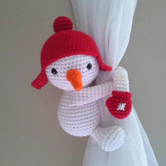 a crocheted snowman hanging from the side of a curtain with a red hat and mittens on