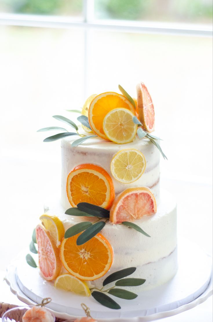 a three tiered cake with orange slices and leaves on the top, sitting in front of a window