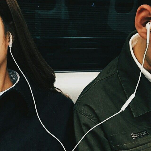 a man and woman sitting next to each other with ear buds in their ears, looking at the camera