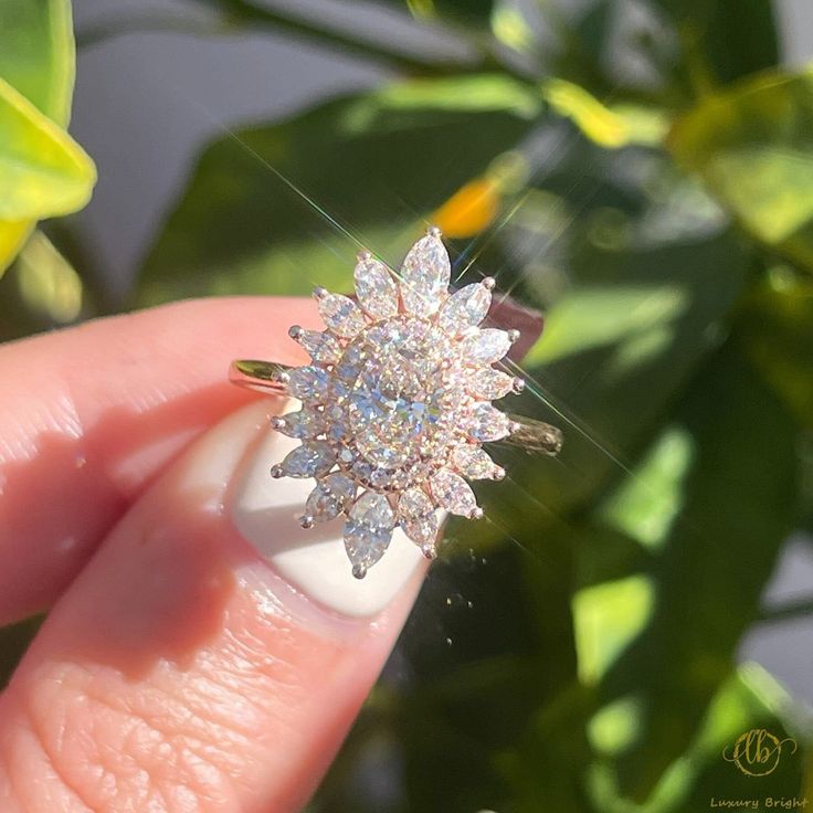 a person holding a ring with diamonds on it's finger in front of a plant