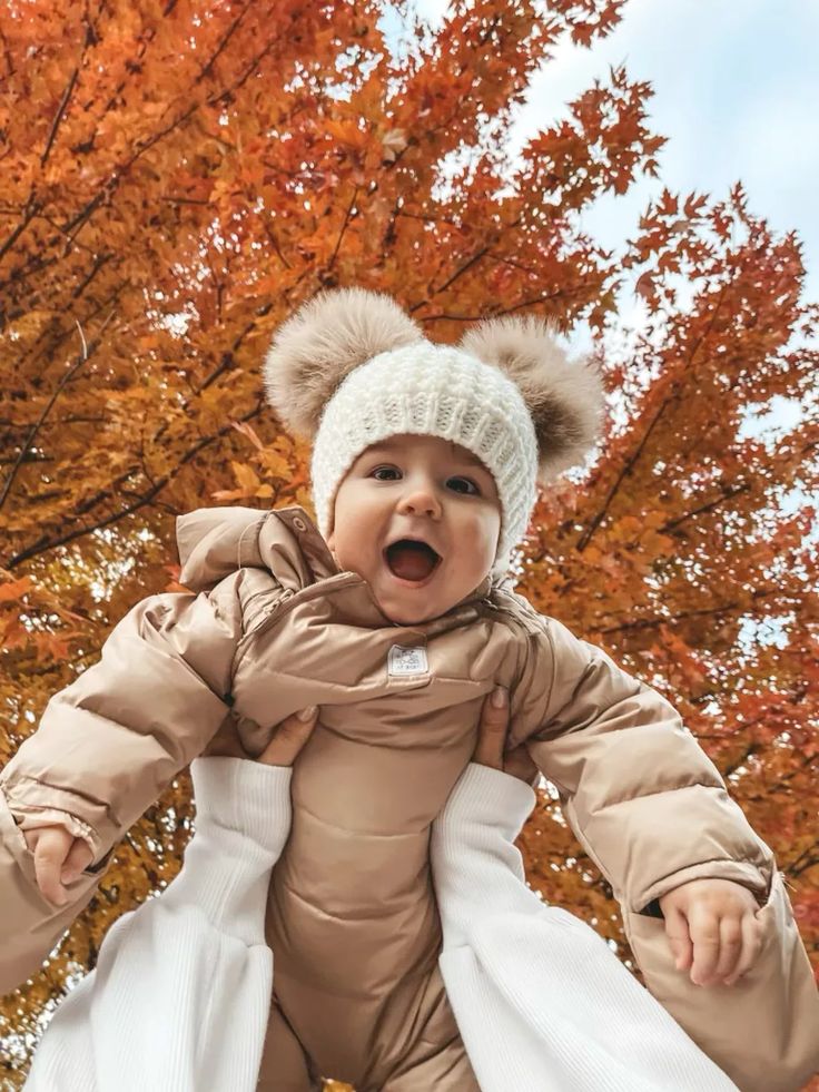 a baby in a bear suit is holding on to an adult's coat and hat