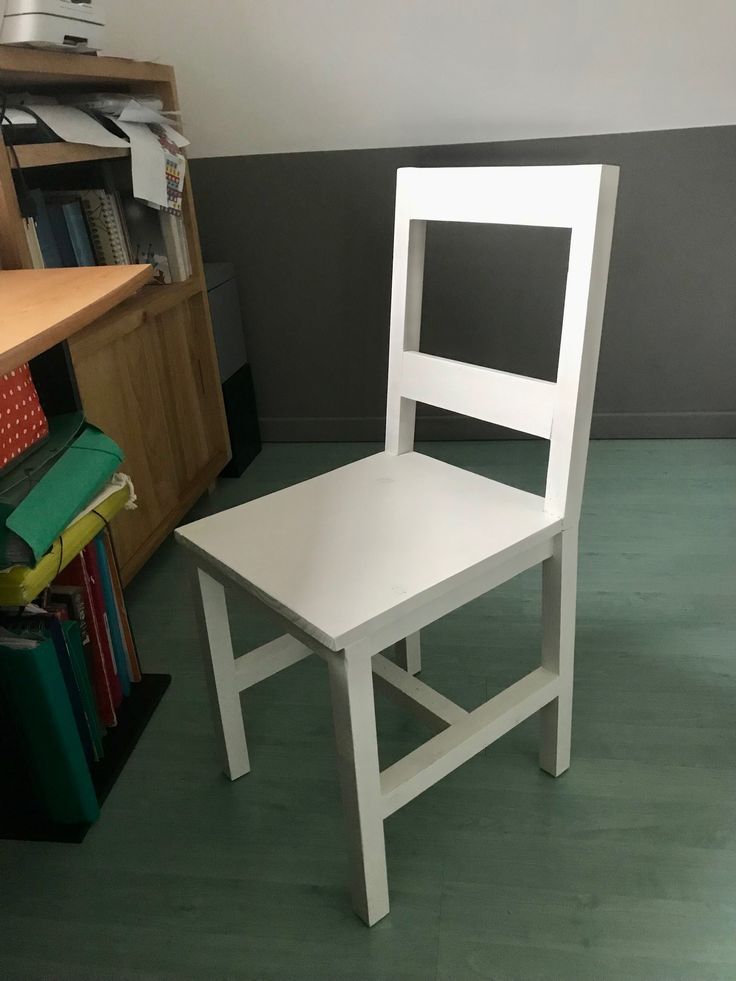 a white chair sitting on top of a green floor next to a bookshelf