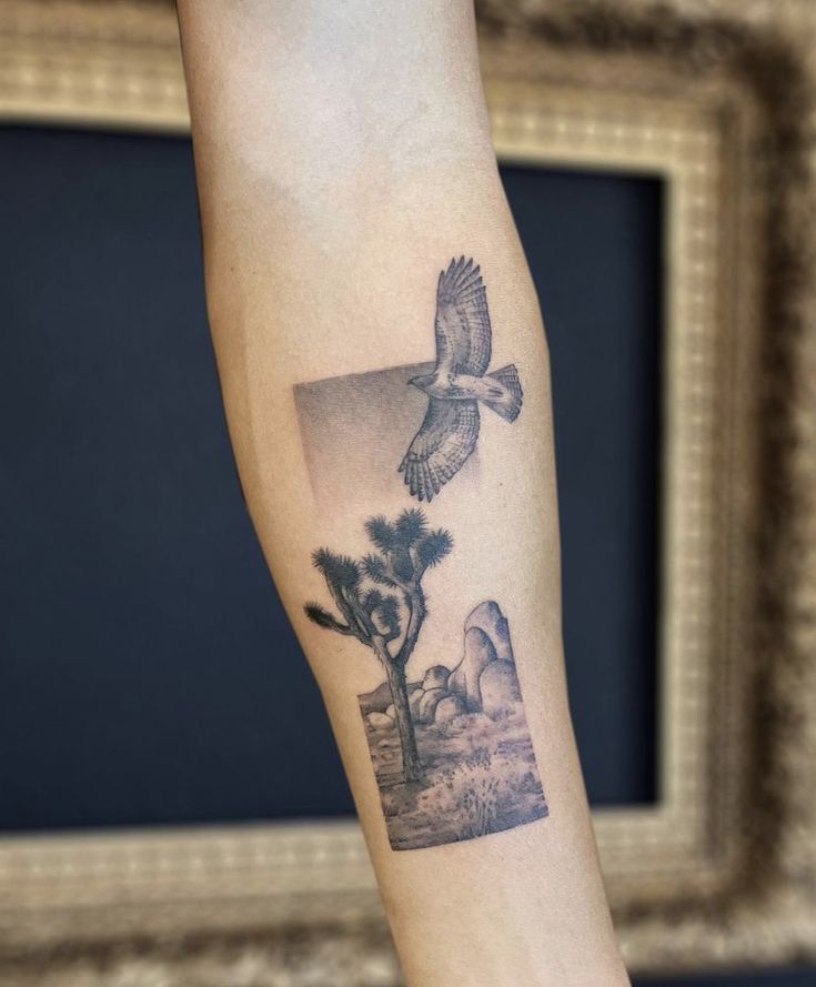 a tattoo on the arm of a person with a bird flying above it and mountains in the background