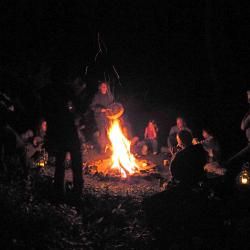 people sitting around a campfire at night with the lights on and one person standing