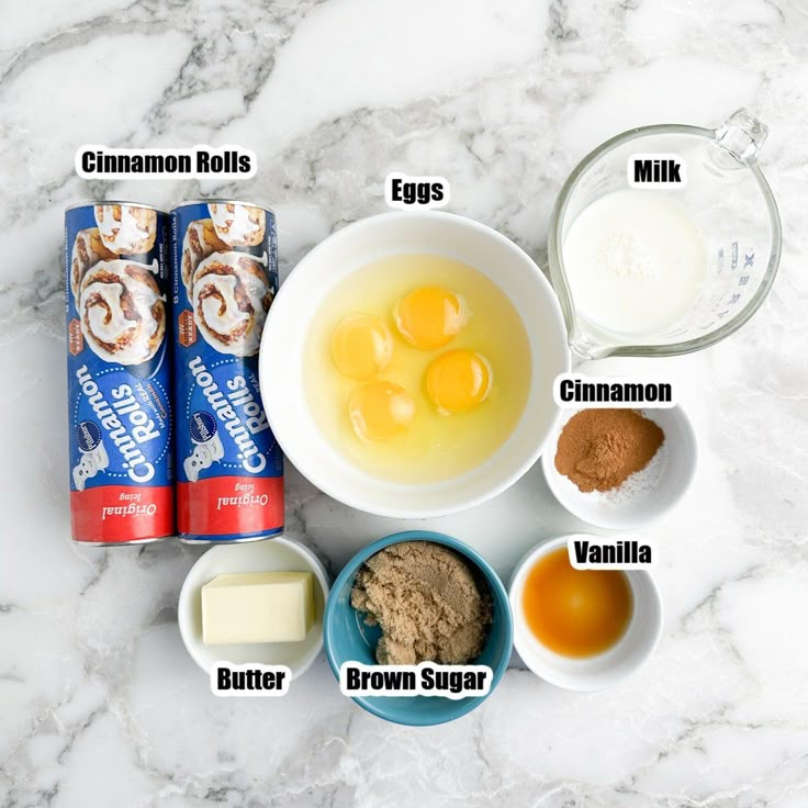 ingredients to make cinnamon rolls laid out on a marble counter top, including milk, eggs, cinnamon, butter, and vanilla