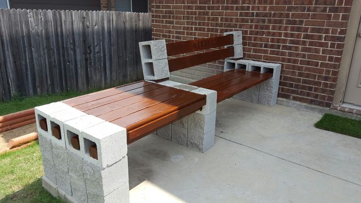 a bench made out of concrete blocks sitting in front of a brick wall and fence