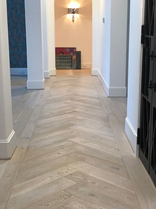 an empty hallway with white walls and wood flooring on the side, leading to another room