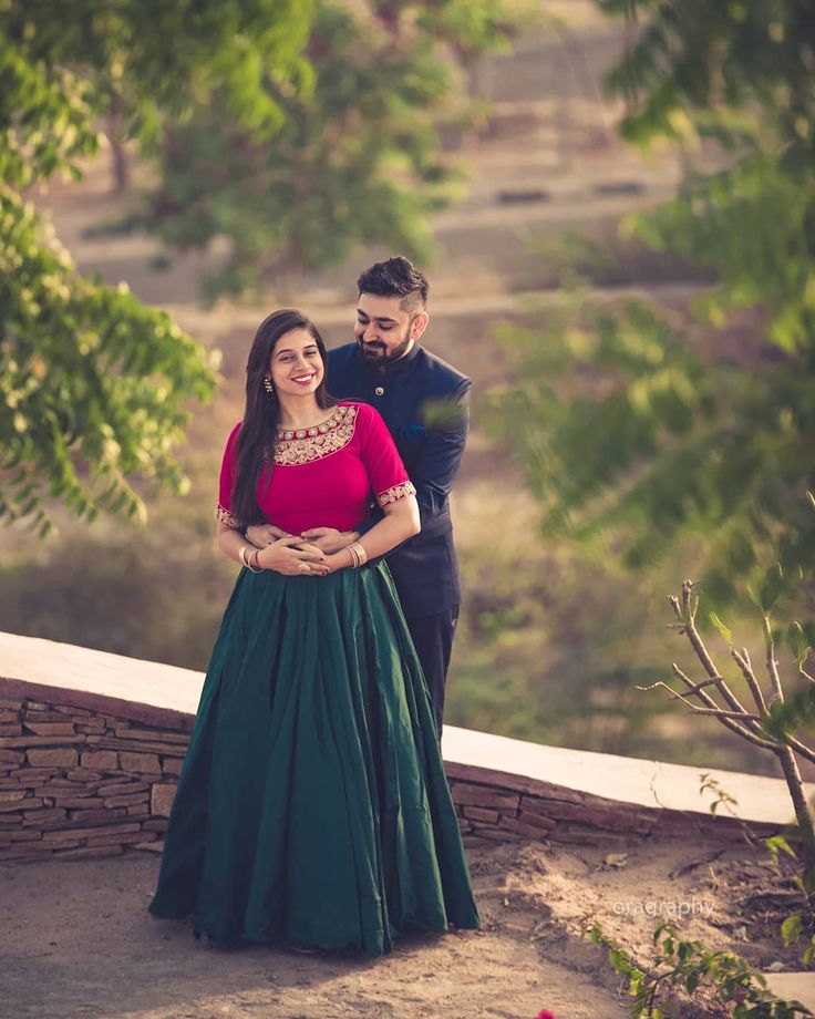 a man and woman standing next to each other in front of some trees, posing for the camera