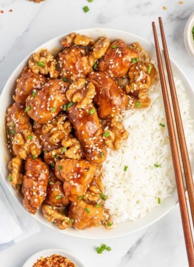 a white plate topped with chicken and rice next to chopsticks