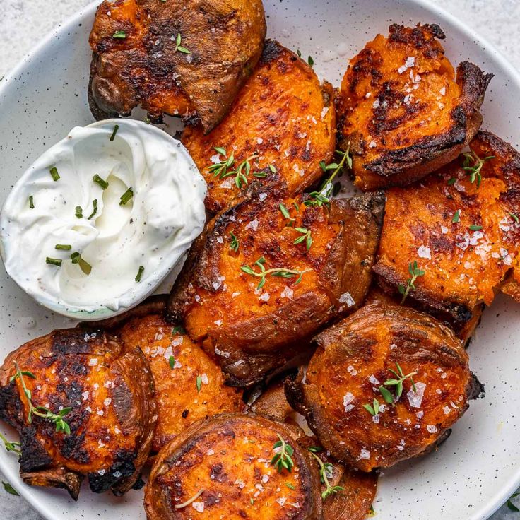 a white plate topped with potatoes covered in sour cream and garnished with herbs