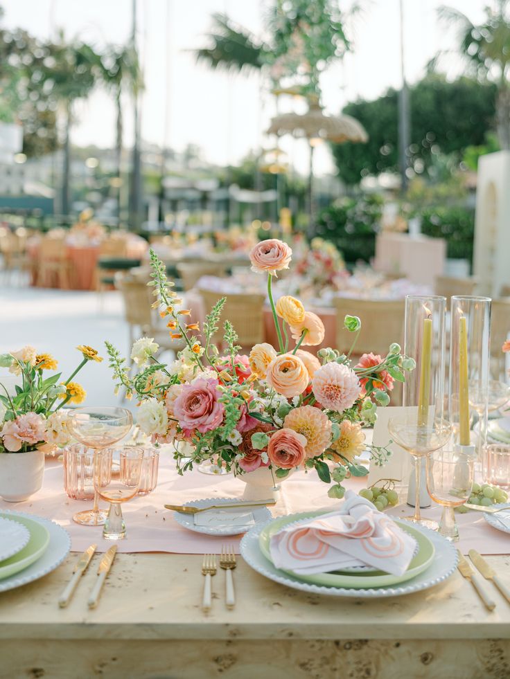 the table is set with pink and yellow flowers in vases, plates and napkins