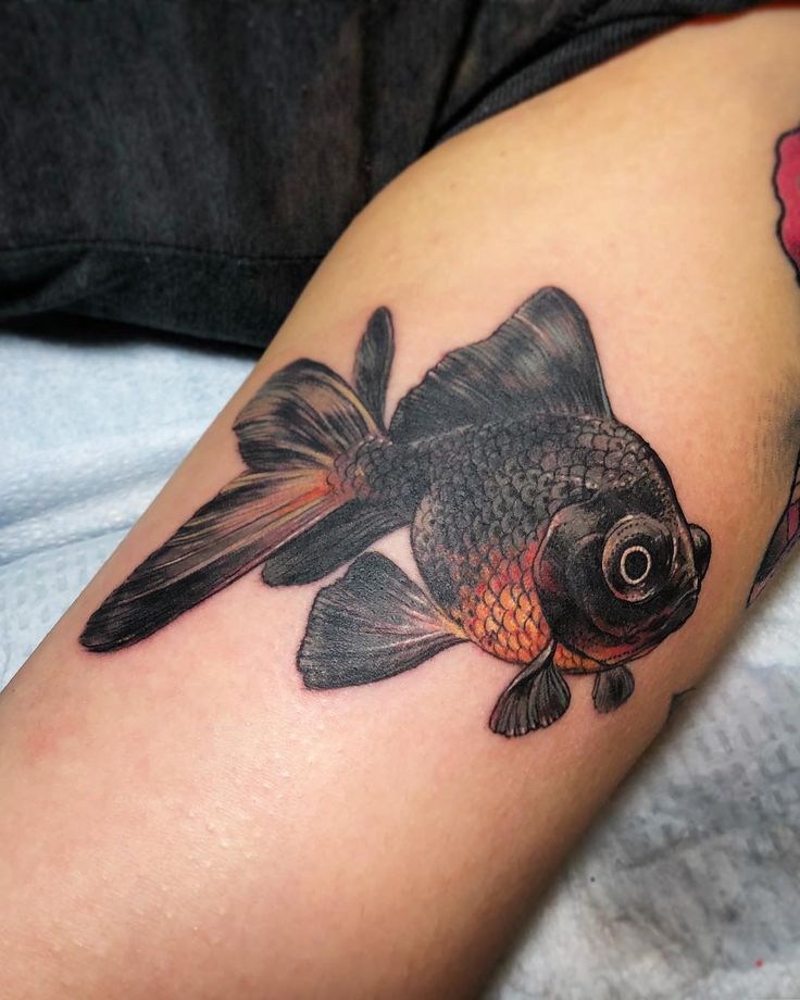 a black and gold fish tattoo on the right arm, with red flowers in the background